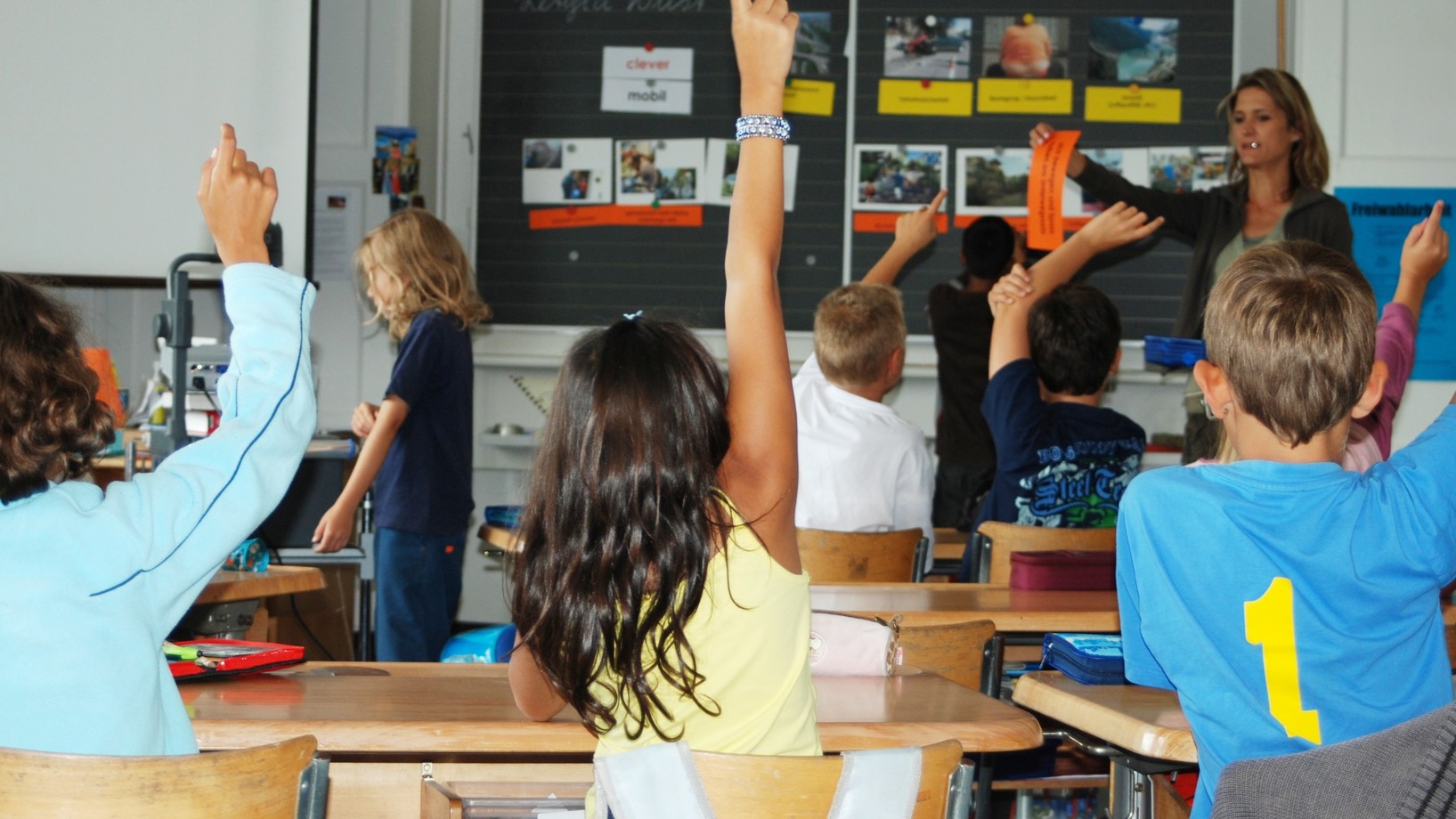 Schulkinder streckend am Pult im Klassenzimmer