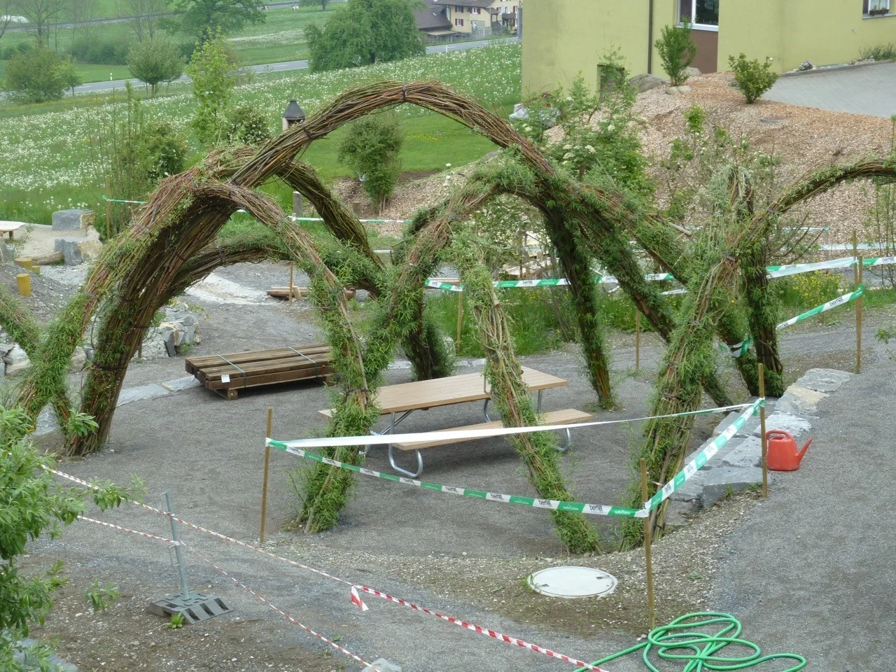 Ein Geflecht aus zusammengebundenen Weidenruten überragt den Sitzplatz