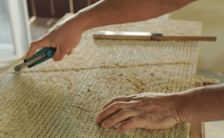 Person schneidet mit Teppichmesser die Lehmbauplatte zurecht
