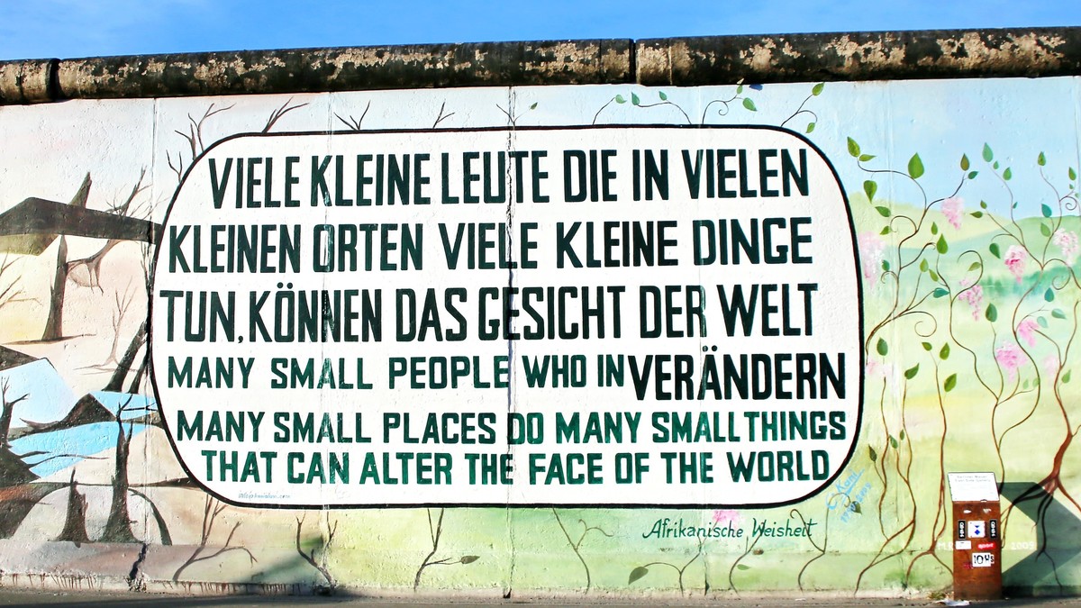 Eine bunt bemalte Mauer mit dem Schriftzug: Viele kleine Leute die in vielen kleinen Orten viele kleine Dinge tun können das Gesicht der Welt verändern.