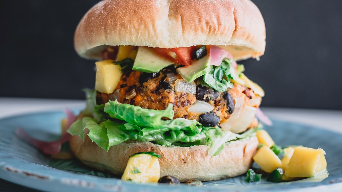 Ein veganer Burger auf einem Teller, vor grauem Hintergrund.