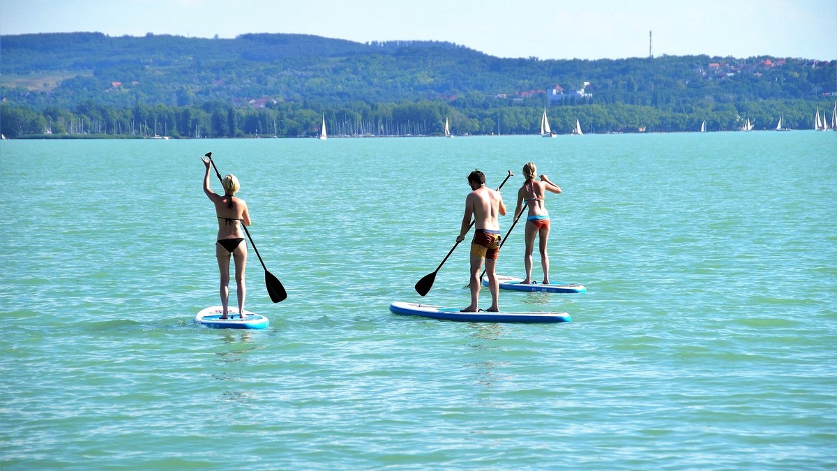 Zwei Frauen und ein Mann beim Stand-up-Paddeln auf einem See