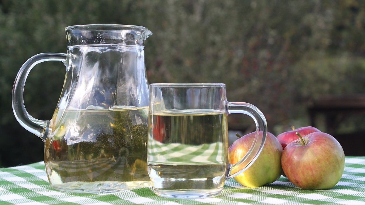 Ein Glaskrug gefüllt mit Apfelsaft steht neben einem gefüllten Glas und zwei Äpfeln