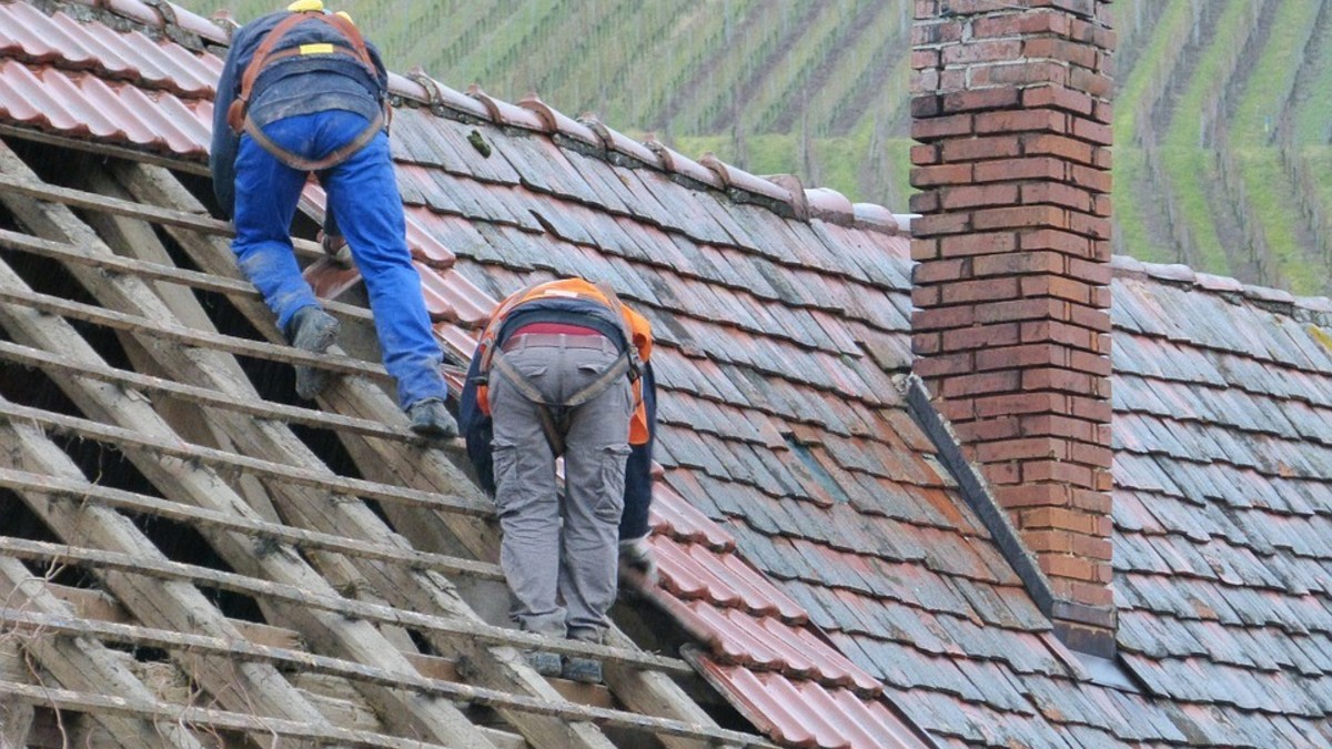 Zwei Handwerker legen neue Ziegel auf ein Dach