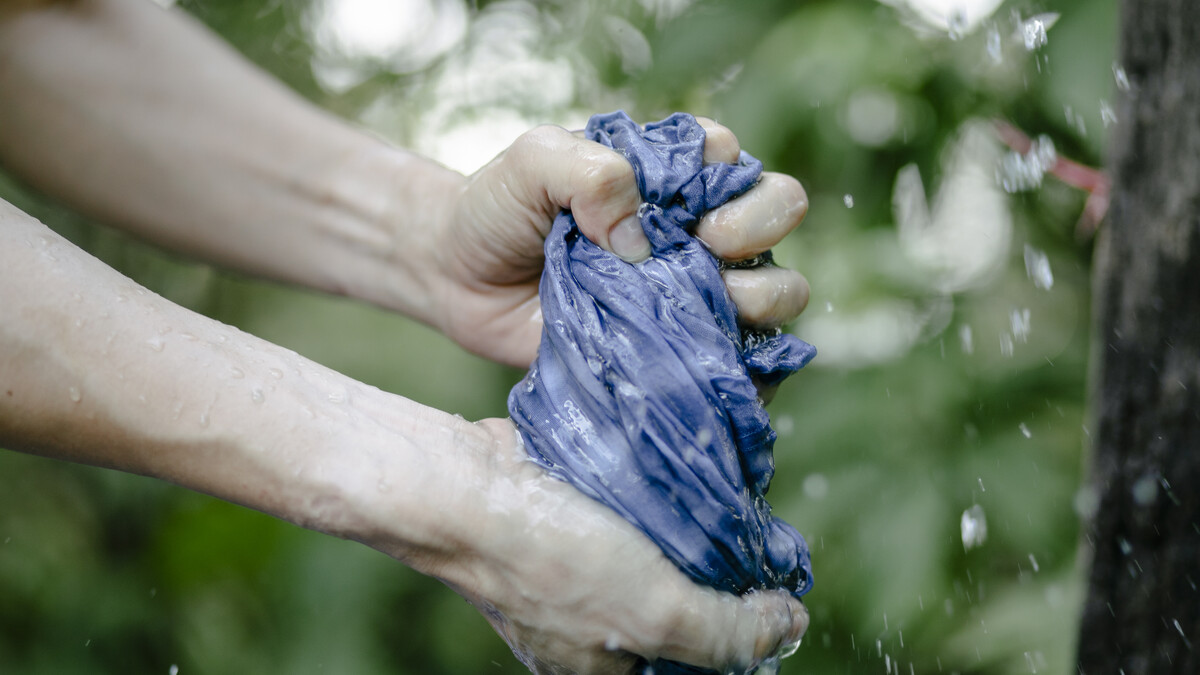 Crop person washing dyed textile