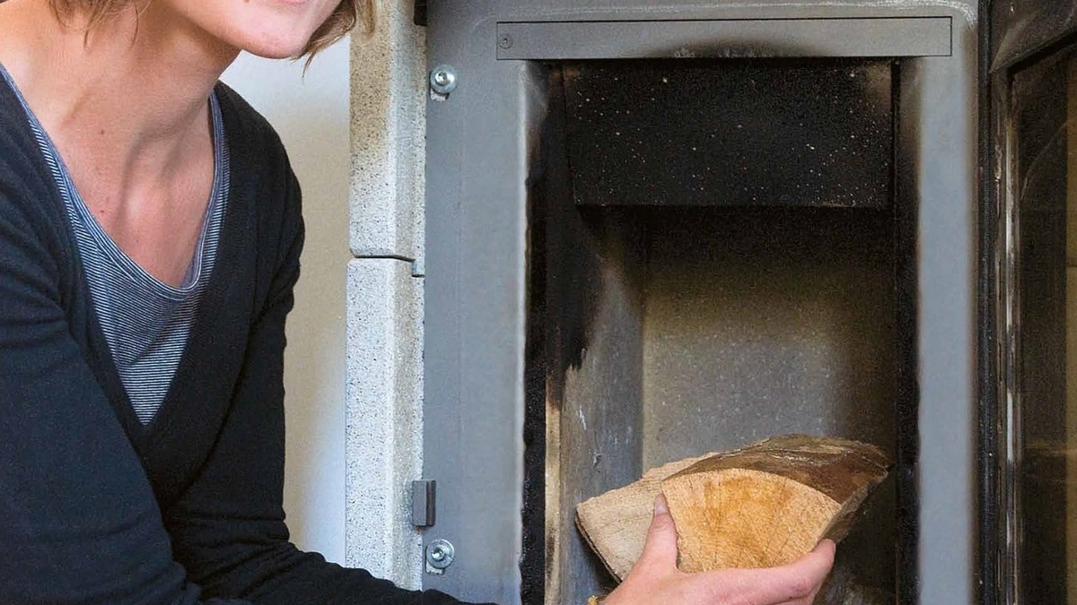 Eine Frau legt Holz in einen Ofen