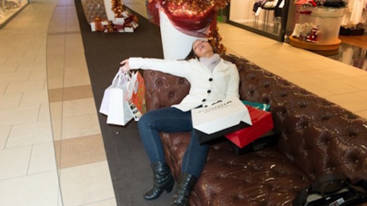 Frau ist müde vom vielen Einkaufen und liegt auf einem Sofa im Kaufhaus