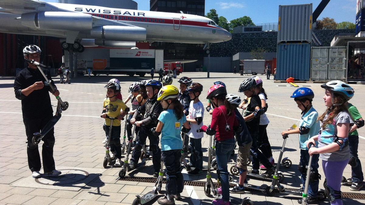 Verschiedene Kinder auf dem Kickboard vor einem Flugzeug im Verkehrshaus Luzern