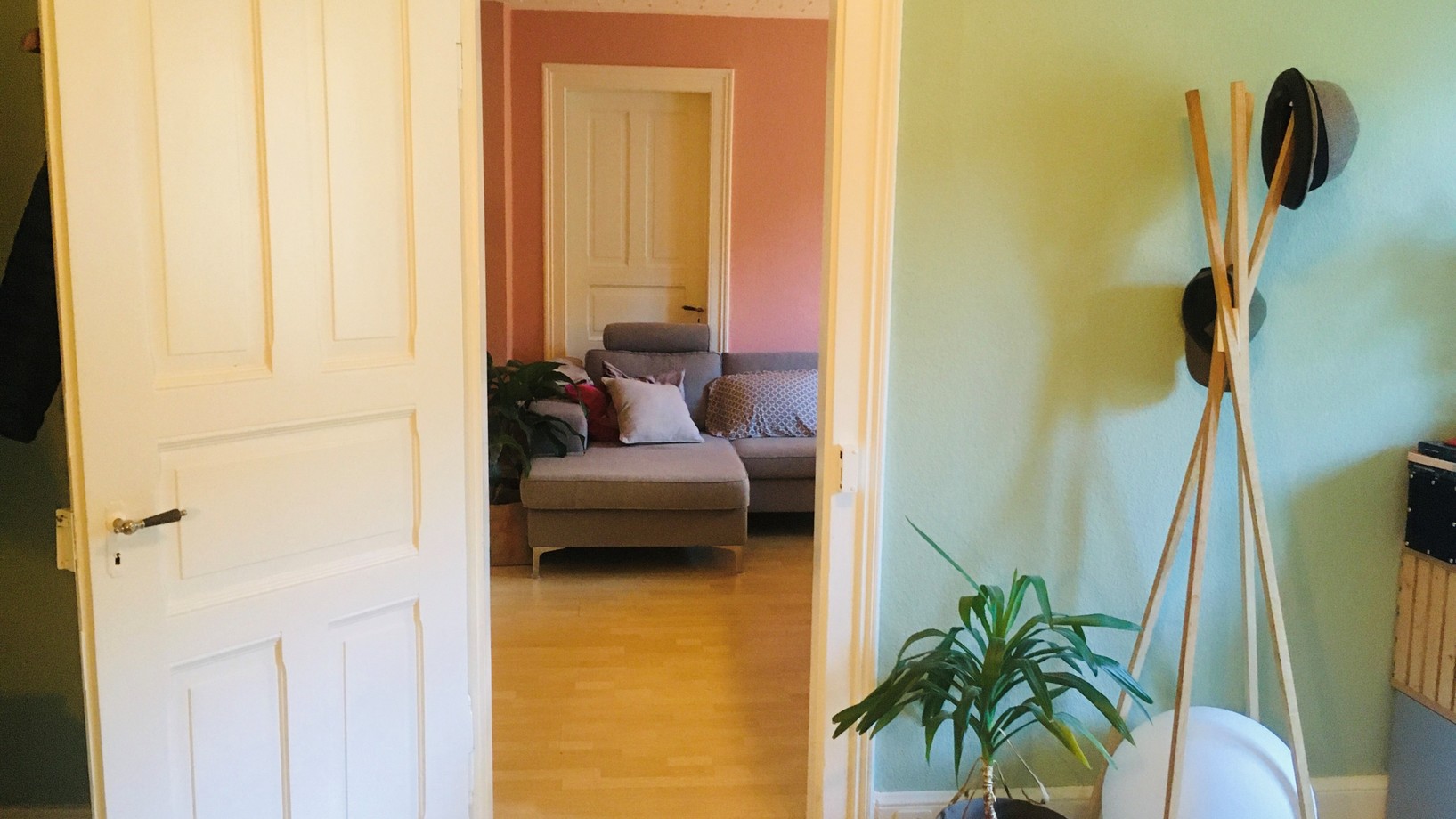 Durch eine weisse Türe sieht man von einem grün gestrichenen Zimmer auf ein altrosa gestrichenes Zimmer
