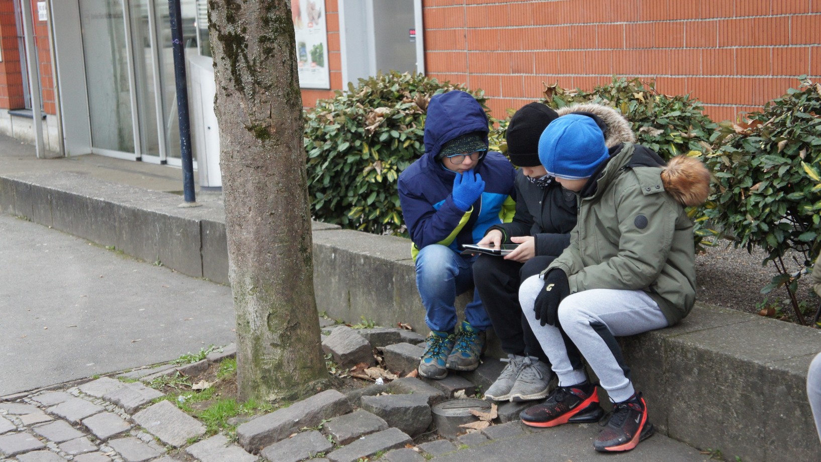 Drei Kinder sitzen auf einer Mauer und versuchen die Fragen zu lösen zu Recycling. 