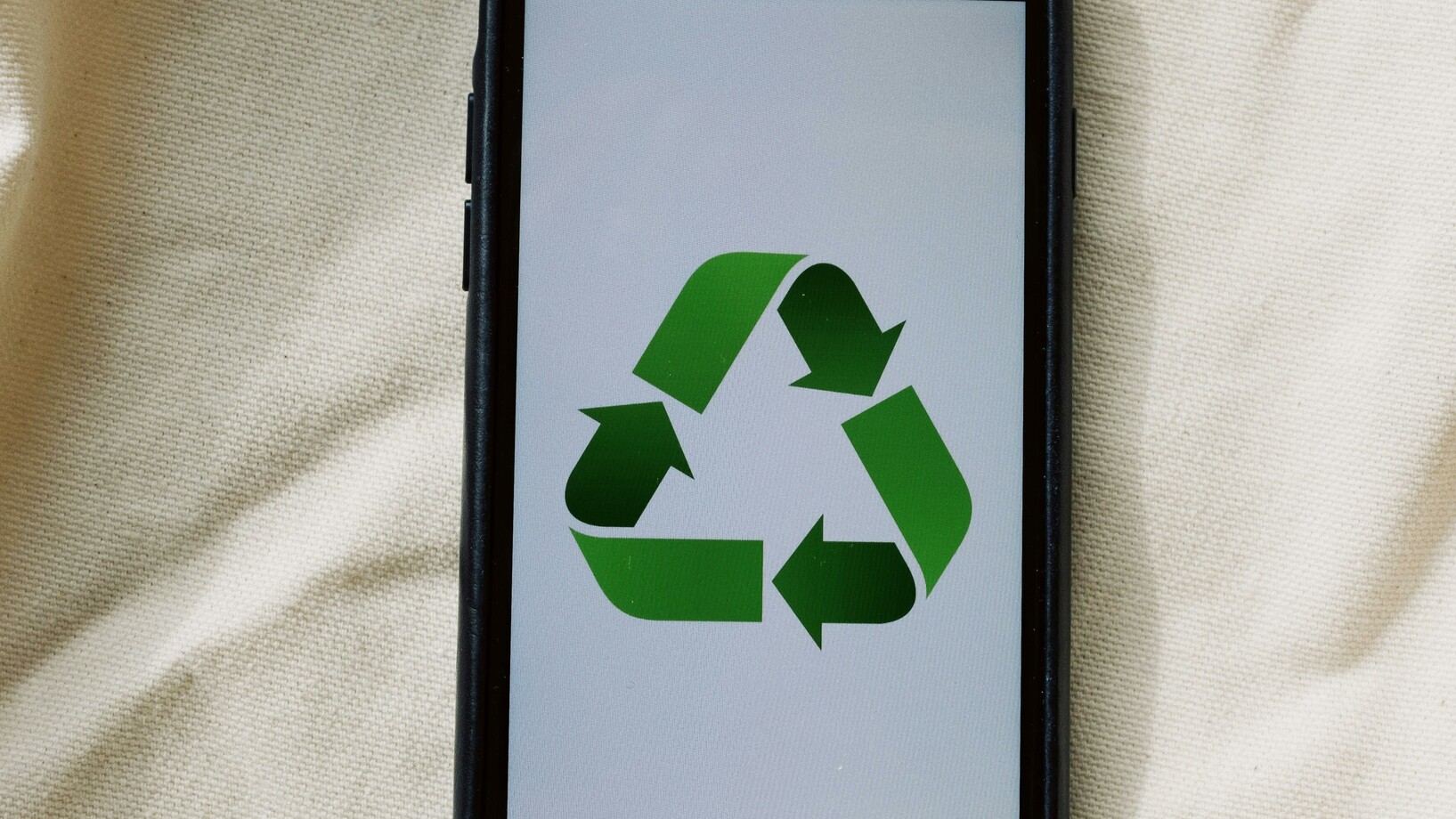 Smartphone with recycling symbol on screen placed on white textile surface
