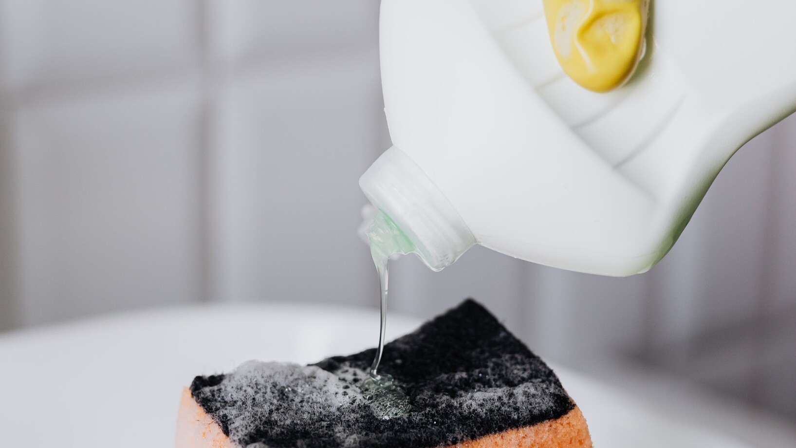 Person in gloves pouring detergent from bottle to sponge