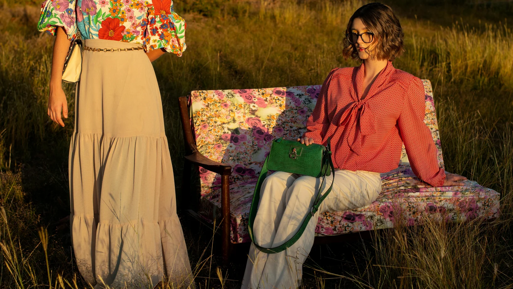 Woman in longsleeve blouse and cream pants sitting on floral couch on grass field