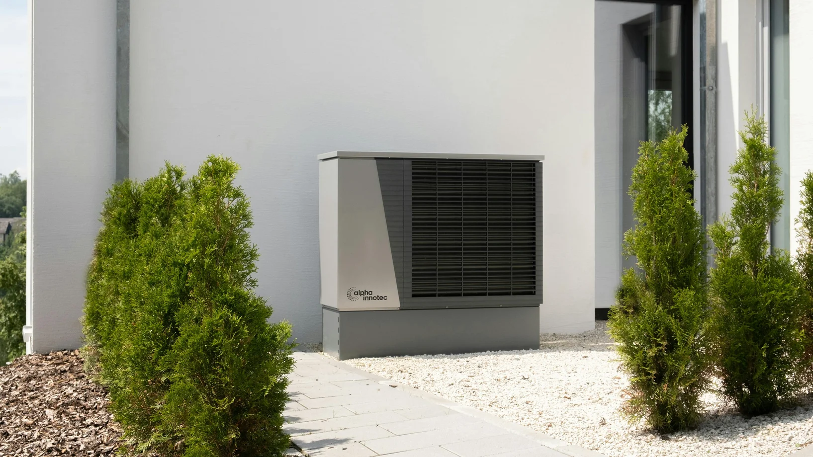 Outdoor air conditioner unit on a modern building surrounded by greenery and landscaping.