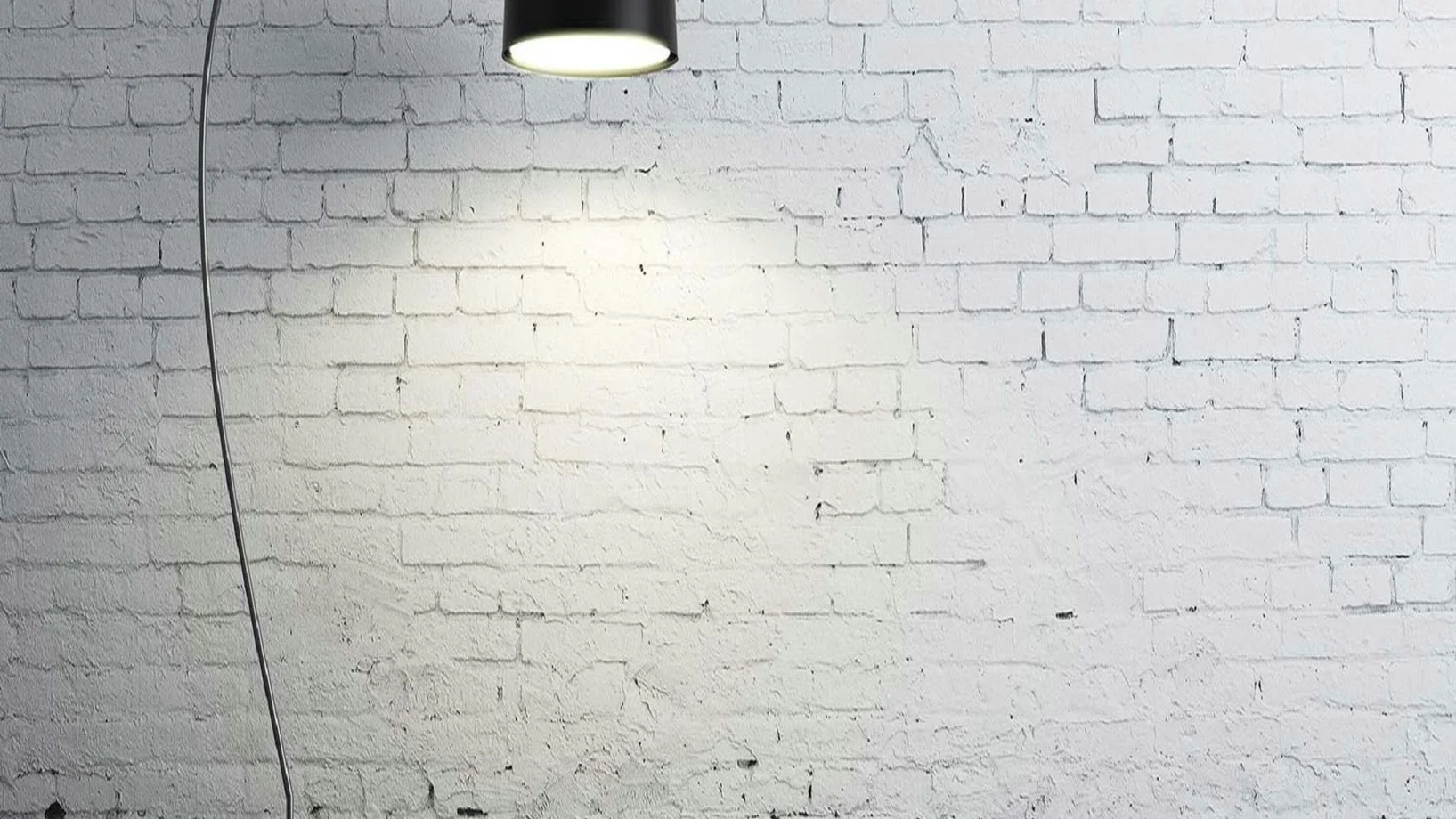 Sleek modern floor lamp casting light on a textured white brick wall.