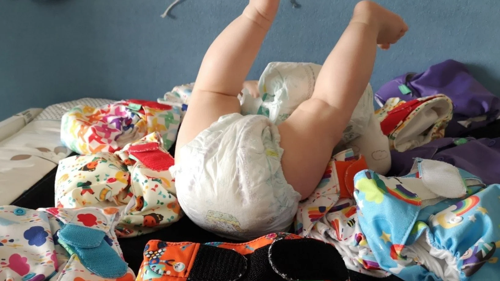 Baby trägt eine Einwegwindel und ist umgeben von Stoffwindeln.